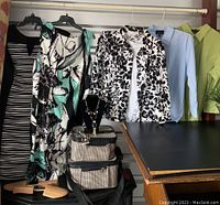Photo of dresses, blouses, packing bag, luggage tag, and shoehorns arranged on and around a table.