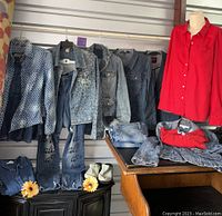Photo shows multiple denim jackets and shirts hanging, several pairs of denim jeans arranged below, and a mannequin wearing a bright red button-up shirt.