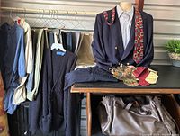 Full lot view showing clothing hanging on rack, folded clothing pieces on table, blazer on mannequin with ties, and leather packing bag below
