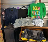 Full lot including hanging shirts, folded shorts and pants on furniture, and packing bag in front