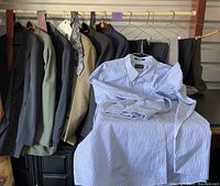 Five men's suits and blue-white pinstriped dress shirt displayed hanging on clothing rack