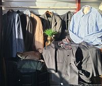 Five men's suits in different colors hung on hangers with pants below and a blue striped shirt on a mannequin, a couple of ties folded and placed on the suits.