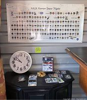 Photo showing NASA Human Space Flight poster with numerous mission logos above a table with sports cards and a clock.