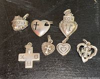 Photo showing seven sterling silver charms or pendants on a black surface with a close-up of different designs including love, crosses, and hearts.