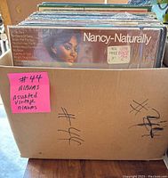 Photo from above showing a cardboard box filled with approximately 44 assorted vintage vinyl albums, noted with handwritten marks and a pink sticky note.
