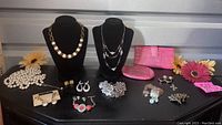 Overview of jewelry including necklaces, clip-on earrings, button covers, and pink wallets on black surface with decorative flowers