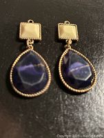 Front view of pair of brass drop earrings with cream square tops and deep blue faceted teardrop stones