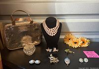 Overall view of jewelry collection including faux pink necklace and earrings, various leaf and rose pins, small heart-shaped box, and metallic blush rose bag.