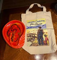 Photo showing the vintage glazed ceramic tray and the canvas bag with The Grapes of Wrath print side by side on a wooden surface.