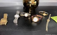 Six vintage watches on black surface showing variety of bands and styles