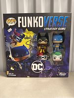 Front of the FunkoVerse DC strategy game box showcasing four exclusive Funko Pop figures inside: Batman, Batgirl, The Joker, and Harley Quinn.