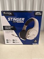 Front of the box showing HyperX Cloud Stinger Core Wireless headphones in white and black with branding and key features like lightweight comfort, steel sliders, wireless, noise cancelling mic, 40mm drivers, and battery life.