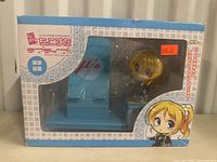 Front view of boxed anime figurine showing character and teal stand with 'μ's' lettering, priced $98