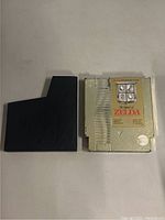 Front view of NES The Legend of Zelda cartridge and black dust cover side by side showing cartridge label and dust cover shape.