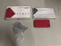 Layout of all items: red Nintendo DSi console, power adapter, original box, manuals.