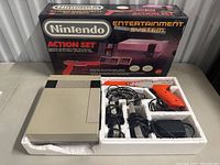 Full view of NES console, Zapper, two controllers, cables and box in background