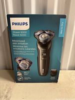 Front side of Philips Shaver 6000 box showing wet & dry shaver, minimized skin irritation feature, MultiPrecision Blade and SkinGuard Mode, included trimming attachment