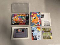 Top view of the game cartridge, box, manuals, and promotional inserts arranged on a flat surface inside a clear plastic protective case.