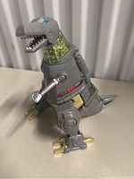Front perspective of gray and metallic robotic dinosaur figure with translucent neck.