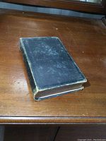 Closed black hardcover book with worn edges on wooden table.