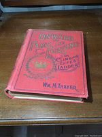Front view of red hardcover book 'Onward to Fame and Fortune or Climbing Life's Ladder' by Wm. M. Thayer showing title text and decorative crown emblem with some wear at edges.