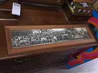 Wide view of the framed panoramic black and white group photograph laid on a wooden surface showing the full length of the frame and photo.