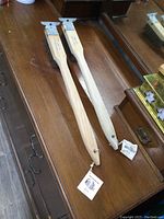 Pair of Felton BBQ brushes laid flat on wooden surface, showing full length of wood handles and tags.