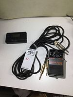 Seiko tuner and Boss pedal with cables arranged on white surface.