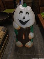 Front view of vintage plastic Halloween blow mold pumpkin figure with smiling face, white pumpkin head, brown body, green stem and leaf accents.