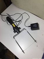 Top view of the wire cutter showing metal frame, wire, and electric cord with power adapter plugged in.
