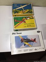 Three boxed model airplane kits: two vintage glider kits (Sap and Mucha) and one plastic SNJ Texan 1:72 scale kit
