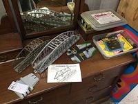 Two metal Warren truss model railroad bridges in silver color, one approximately 14 inches and the other 18 inches long, placed on wooden dresser with instruction sheet visible
