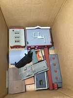 Top-down view showing multiple model railroad buildings of varying sizes and colors packed in a box, including industrial and residential style models.