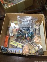 Cardboard box containing multiple packages of HO scale model railroad figures, animals, cars, and various accessories mostly in their original packaging.