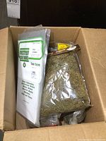 Box containing several sealed bags of Evergreen Scale Models sheet styrene, a bag of green railroad foliage, and other materials for model building.