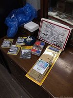 Lot contents on wooden surface including boxed Greenmax kit, several small packages of HO scale structure parts and diecast pieces, with a blue plastic bag in background.