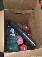 Box open displaying multiple jars and bags of model railroad turf and ballast supplies with a rolled mat on top.