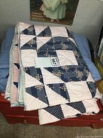 Folded quilt showing outer patchwork of navy blue, pink, and cream fabrics with geometric patterns.