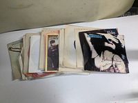 Top view of a stack of over 20 vintage 45 RPM vinyl records in various sleeves, including a visible Scorpions record with the title 'Believe in Love'
