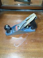 Full side view of Stanley hand plane with blue body, black front knob and rear handle on wooden surface.