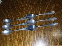 Six sterling silver spoons laid out on a wood grain surface, showing overall length and design details.