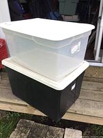 Two plastic totes stacked, clear top tote with white lid, black bottom tote with white lid and wheels
