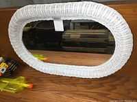 White wicker oval mirror placed on a wooden surface, showing the full mirror and wicker frame