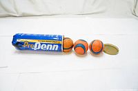 Three orange and blue rubber tennis balls partially inside original blue Pro Penn case with gold text and metal cap