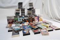 Wide view of numerous audio cassette tapes arranged in stacks and rows on a white surface, showcasing the variety of tape covers and cases.