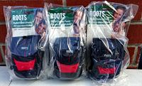 Three new Roots digital camera pouches in original packaging with black and red color scheme hanging on a hook against brick background.
