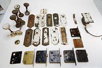 Full lot of antique door hardware laid out including door knobs, backplates with keyholes, and lock mechanisms.