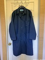 Full front view of navy blue coat hanging on a hanger against a door, showing long sleeves, collar, and button details.