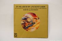 Front cover of the Absolute Elsewhere In Search Of Ancient Gods vinyl LP album depicting abstract artwork on yellow background with album title.