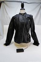 Front view of black soft leather women's jacket on mannequin, fully zipped and showing chain-attached wallet below right pocket.